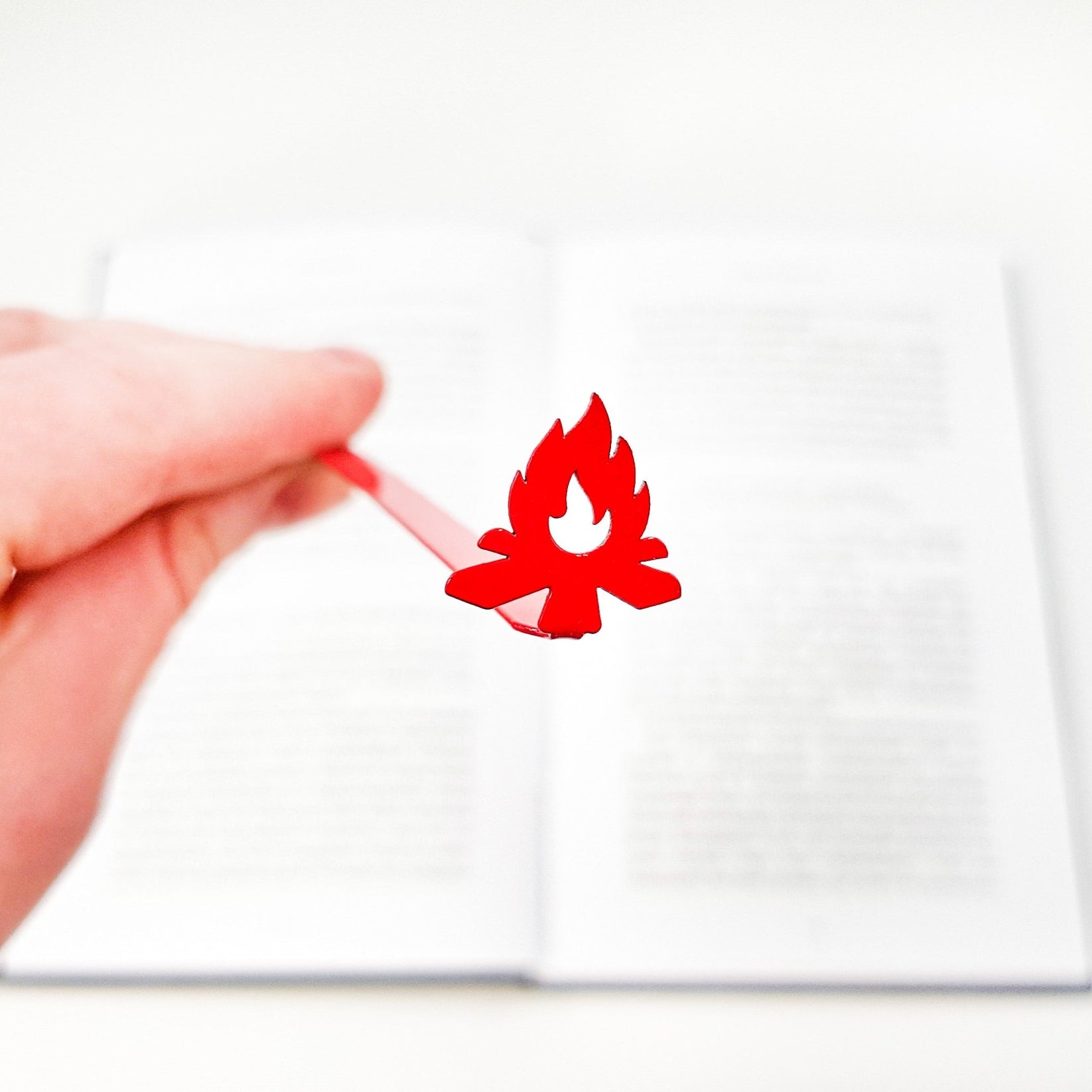 Bonfire metal bookmark in red held in a hand above an open book