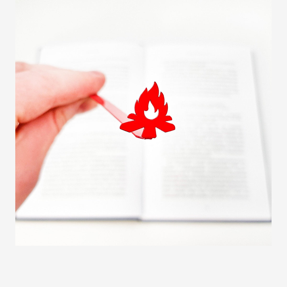 Bonfire metal bookmark in red held in a hand above an open book