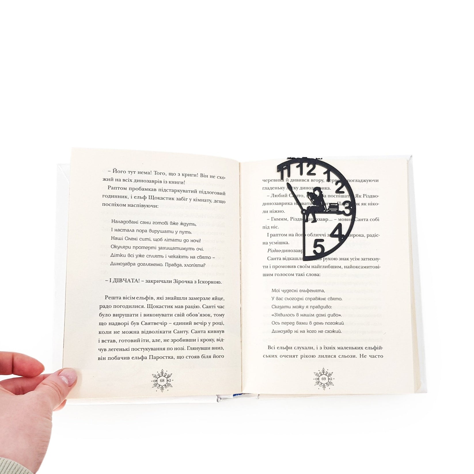 Black metal Book O’Clock bookmark clipped onto an open book, showing the clock-shaped design with a reading figure marking the page on a white background.