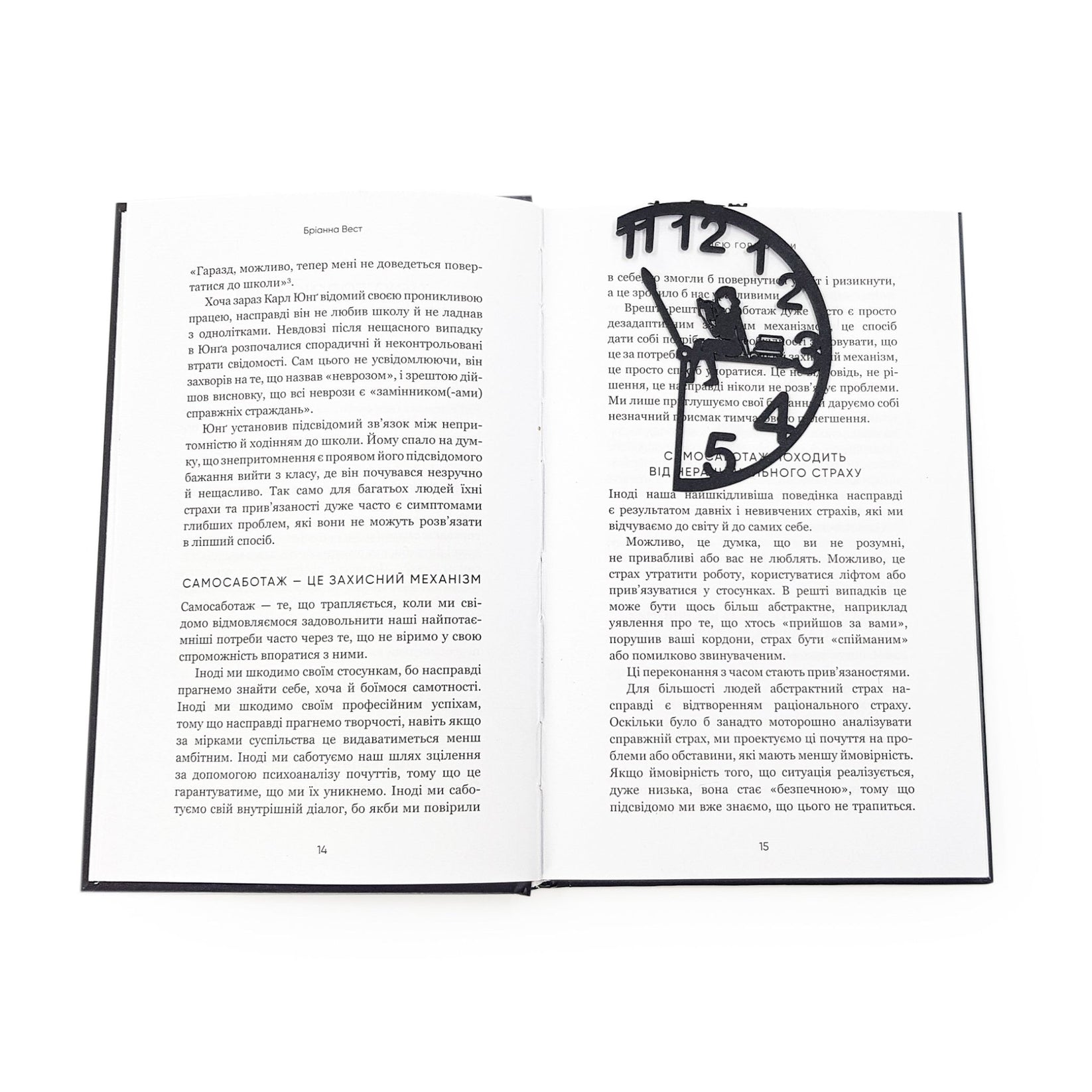 Black metal Book O’Clock bookmark marking a page in an open book, showing the clock-shaped design with a seated reading figure against a white background.