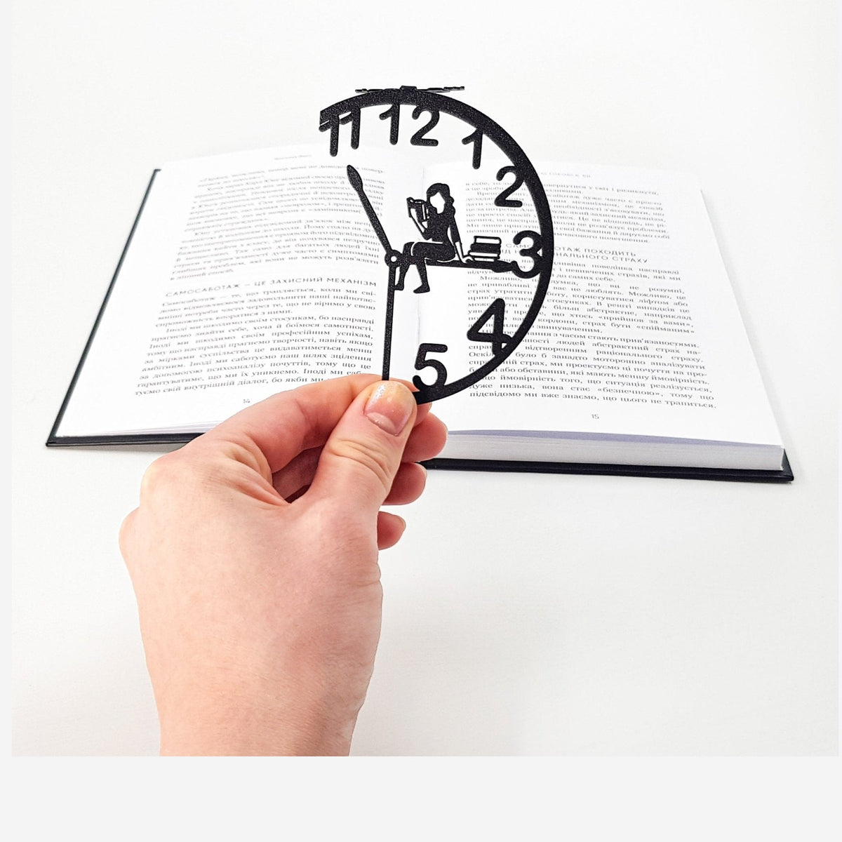 Book O’Clock metal bookmark held in a hand above an open book