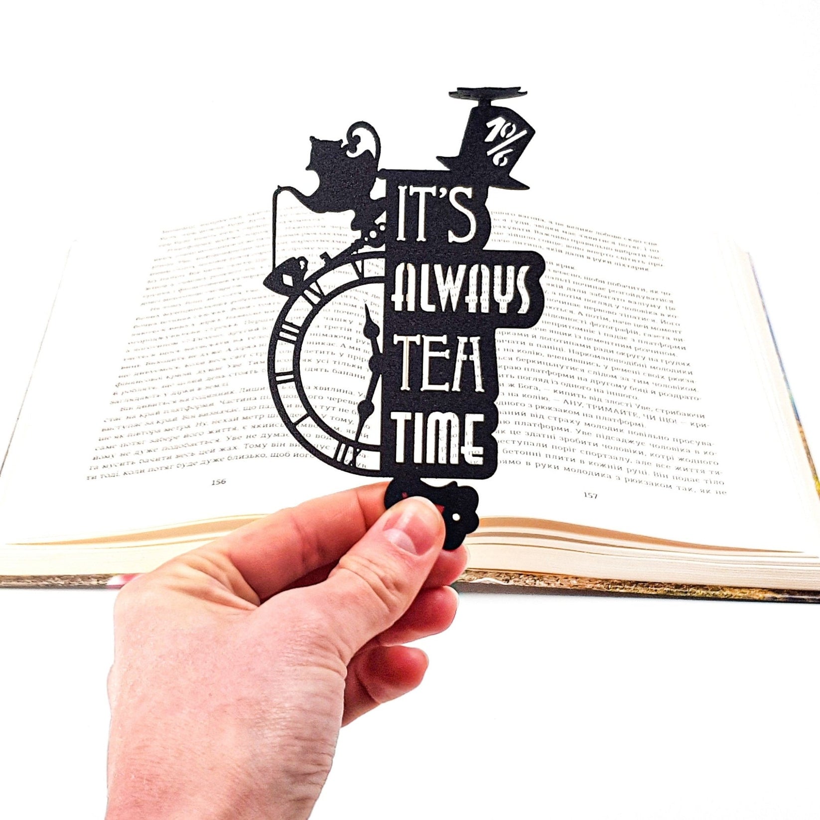 Alice in Wonderland's The Tea Party metal bookmark held in a hand above an open book