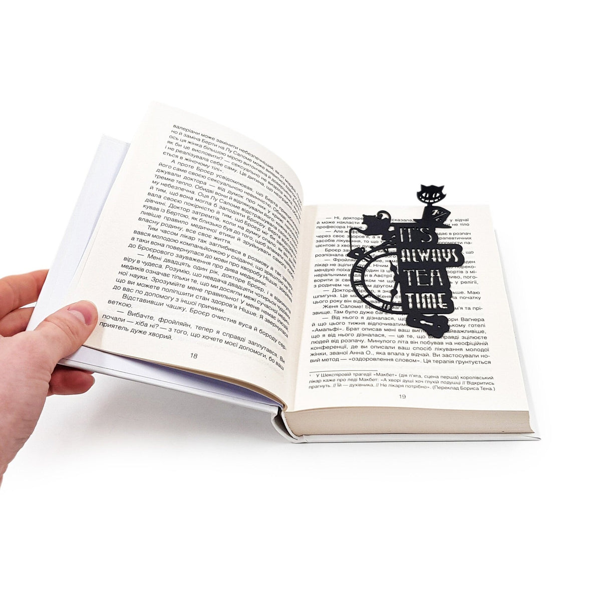 Alice in Wonderland's The Tea Party metal bookmark held up beside an open book