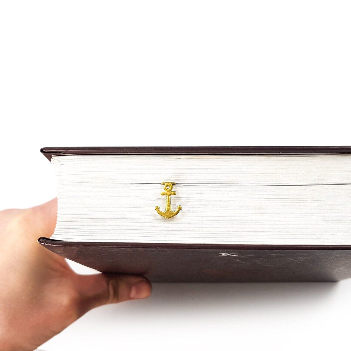 Anchor metal bookmark in gold clipped in a closed book, viewed from the side