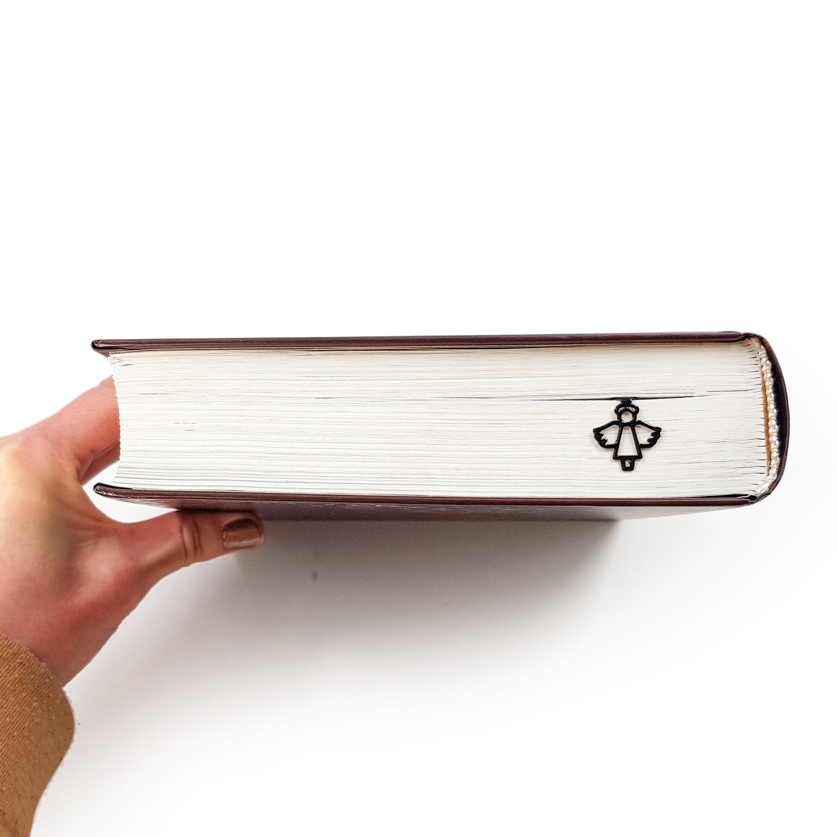 Angel metal bookmark in gold in a closed book, only its top showing above the pages