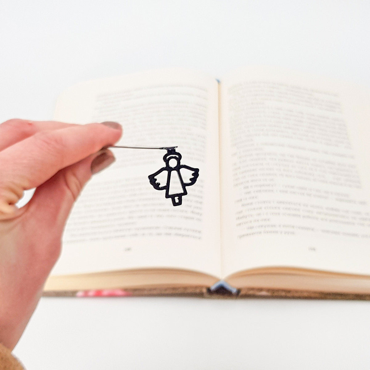 Angel metal bookmark held up beside an open book
