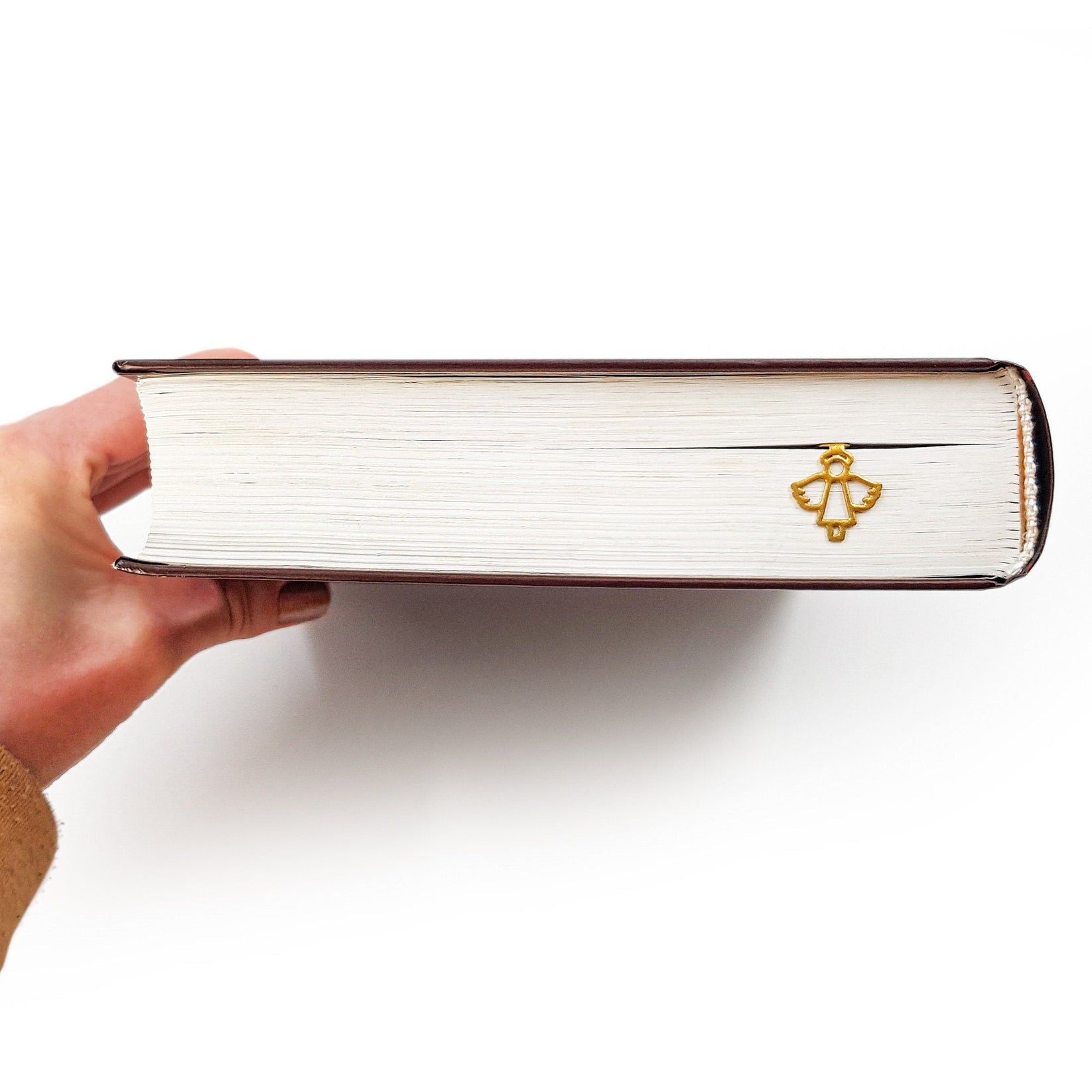 Angel metal bookmark in gold seen from the edge of a closed book
