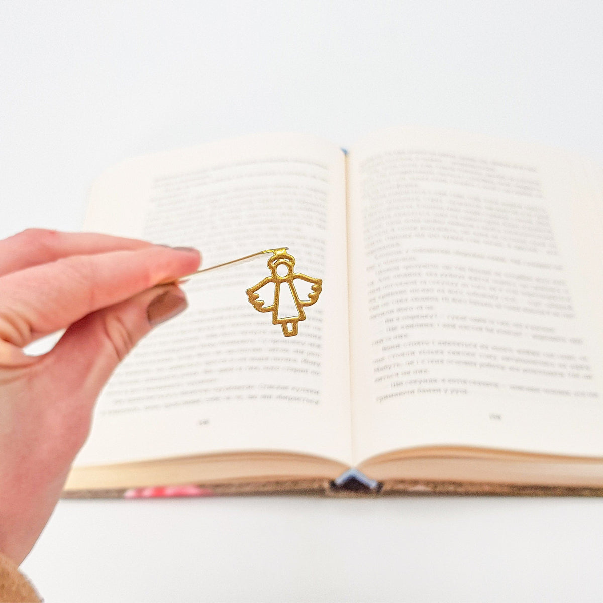 Angel metal bookmark in gold held in a hand above an open book