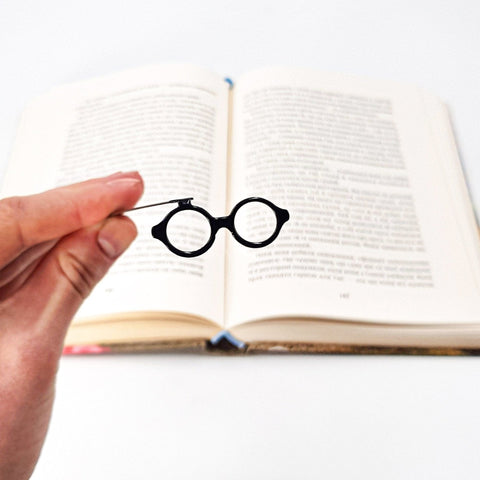 Architect's Eyeglasses metal bookmark held in a hand above an open book