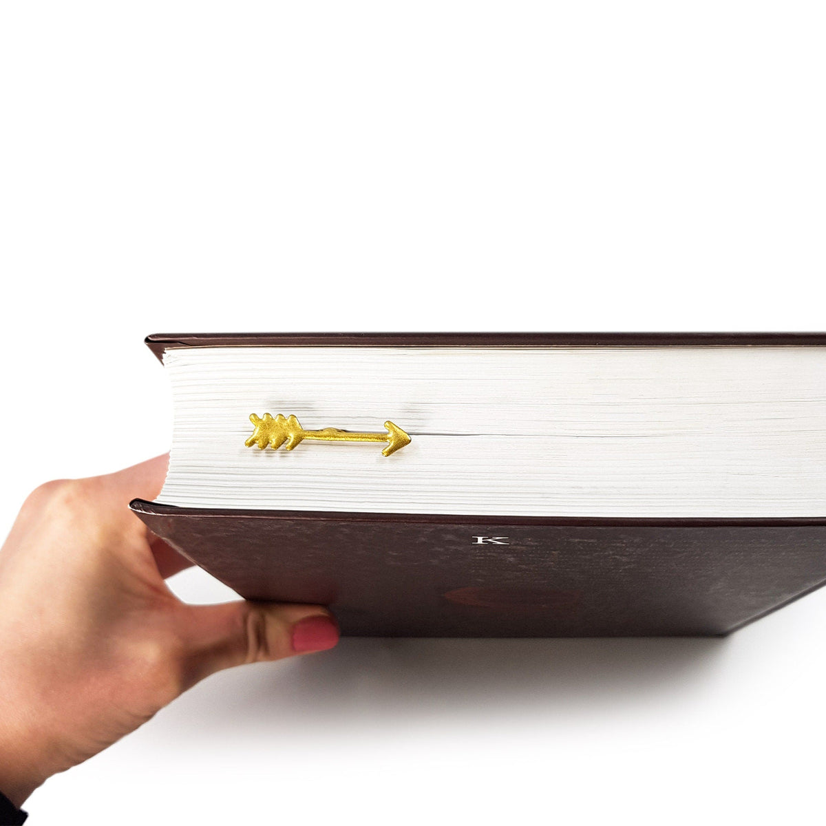 Arrow metal bookmark in gold seen from the edge of a closed book