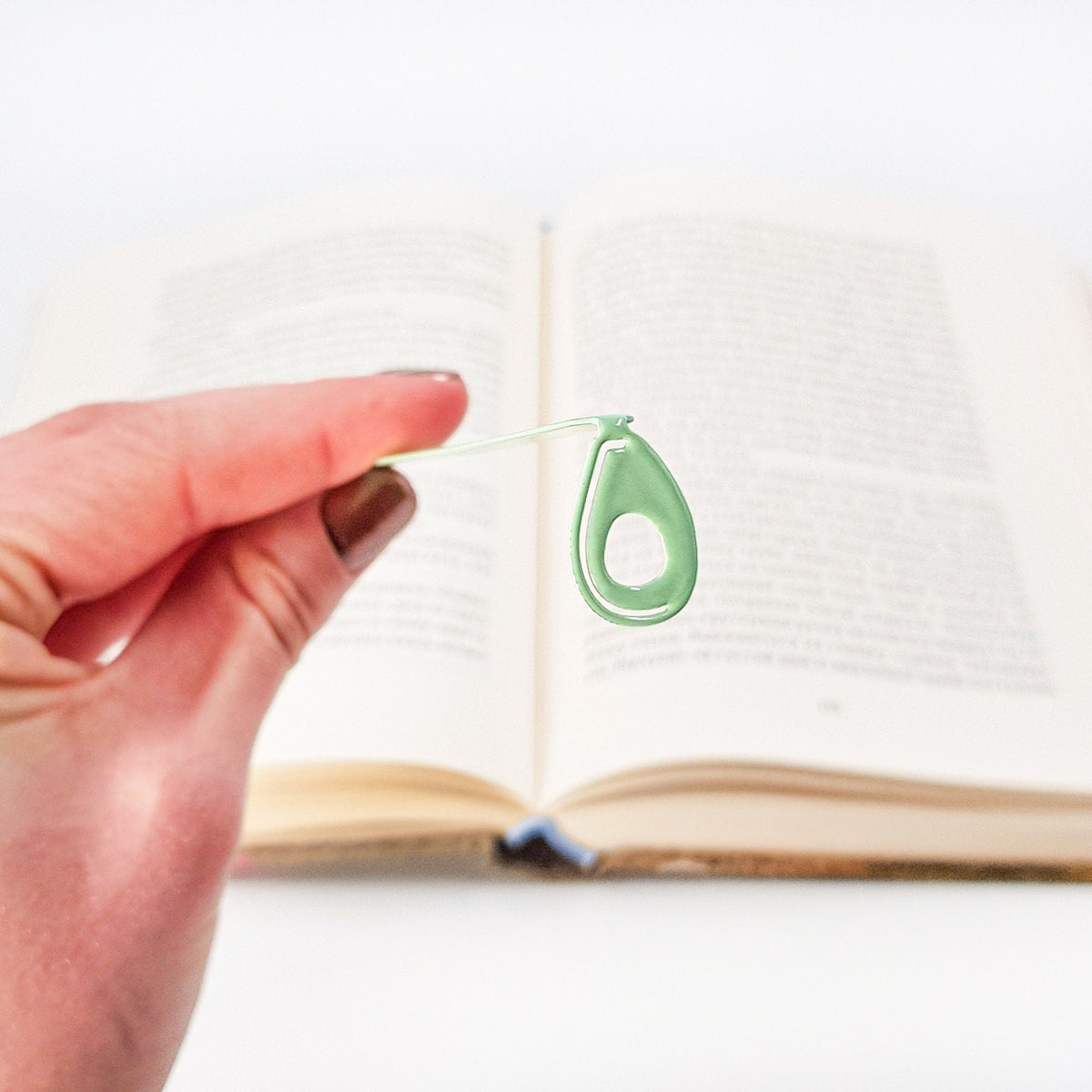 Avocado metal bookmark in green held in a hand above an open book