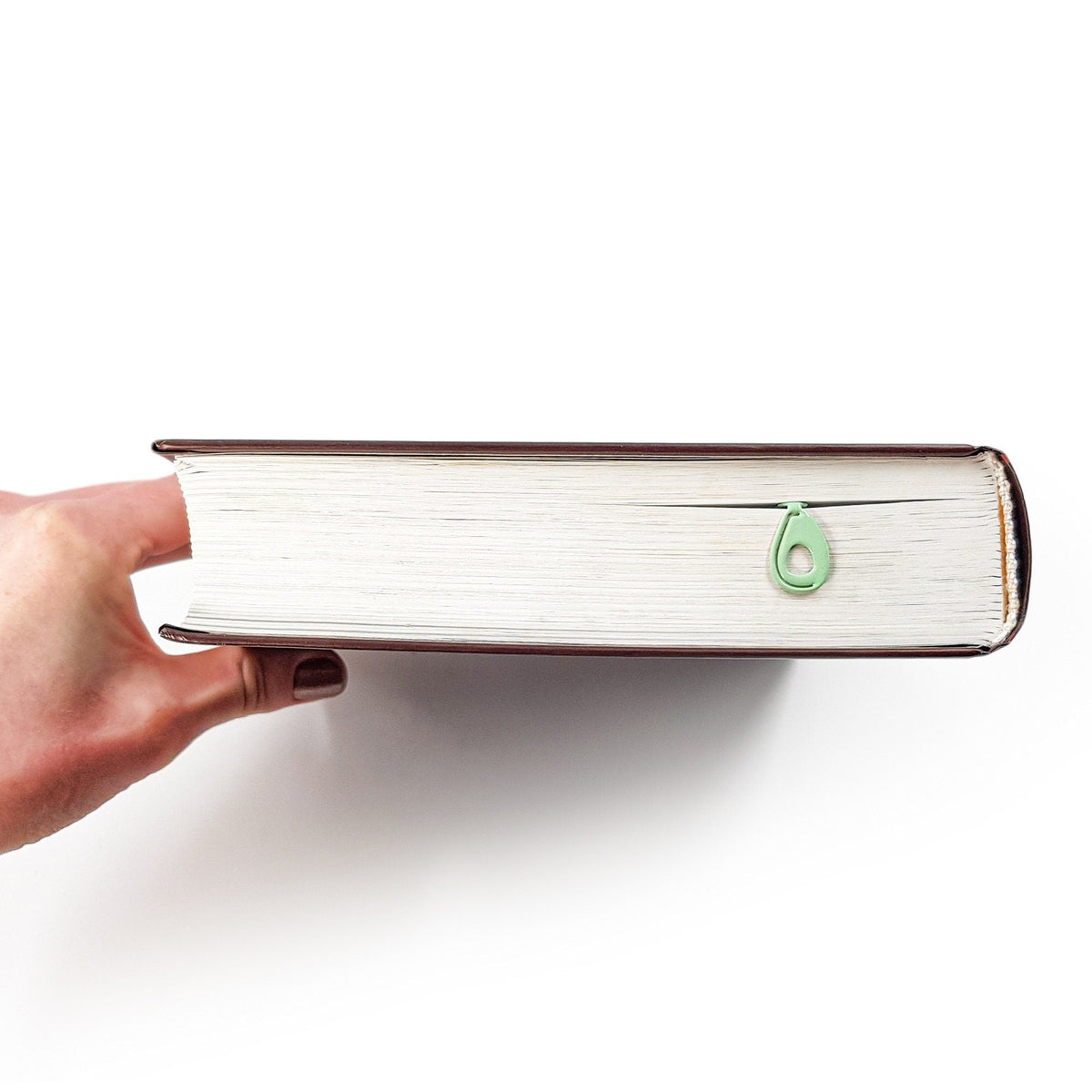Avocado metal bookmark in green in a closed book, only its top showing above the pages