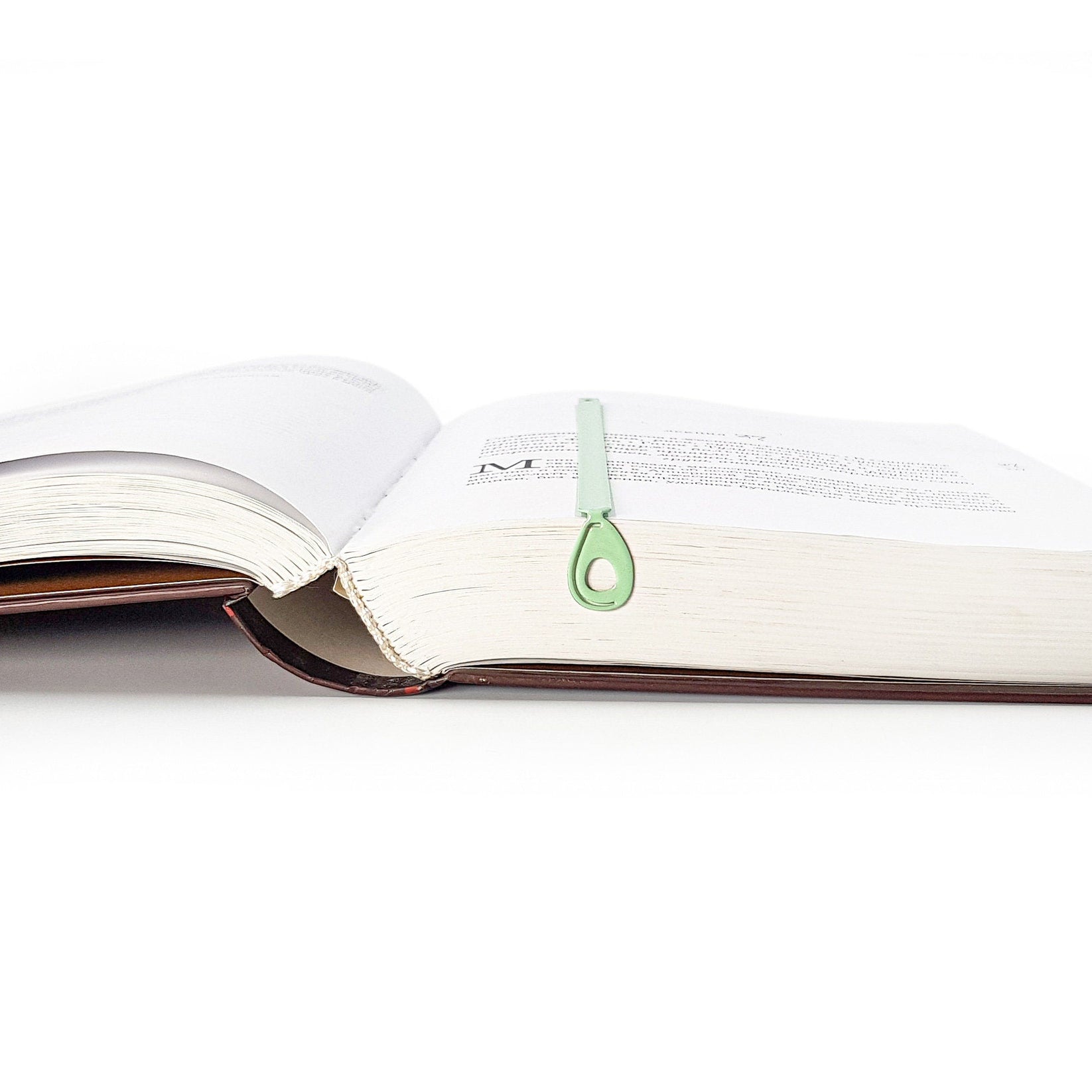 Avocado metal bookmark in green marking a page in an open book