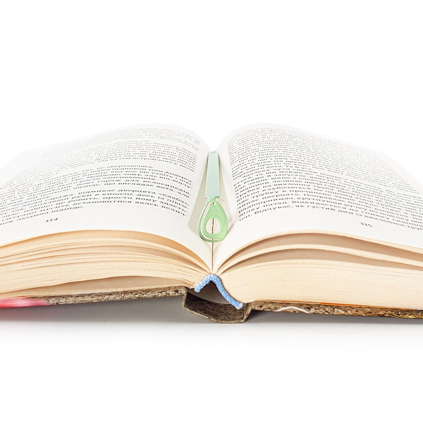 Avocado metal bookmark in green lying across the pages of an open book