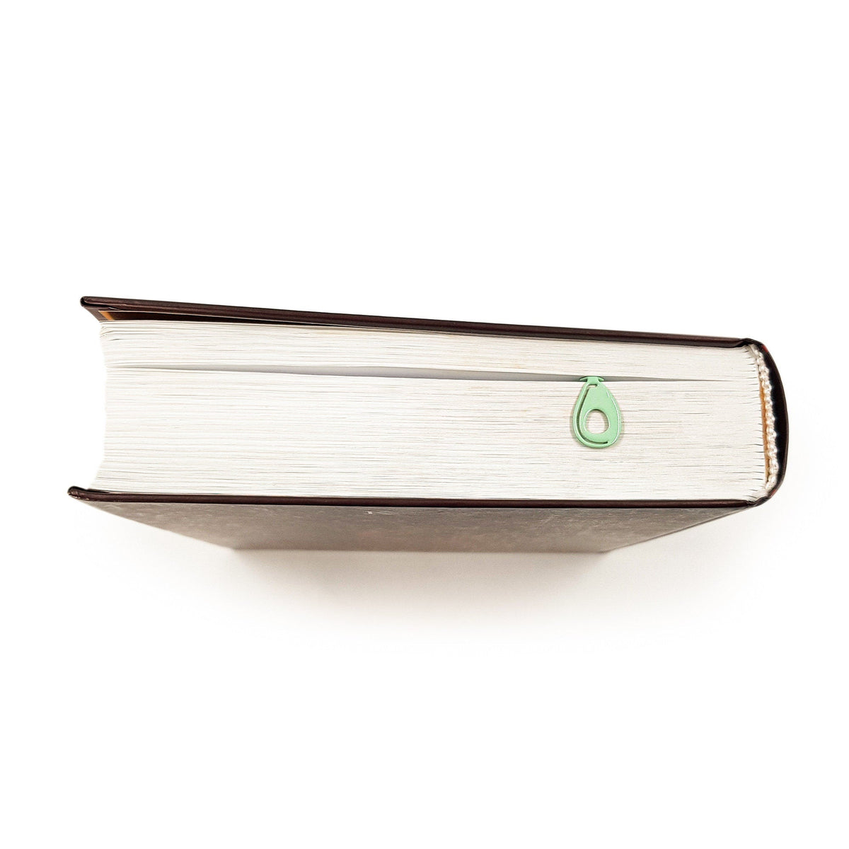 Avocado metal bookmark in green seen from the edge of a closed book