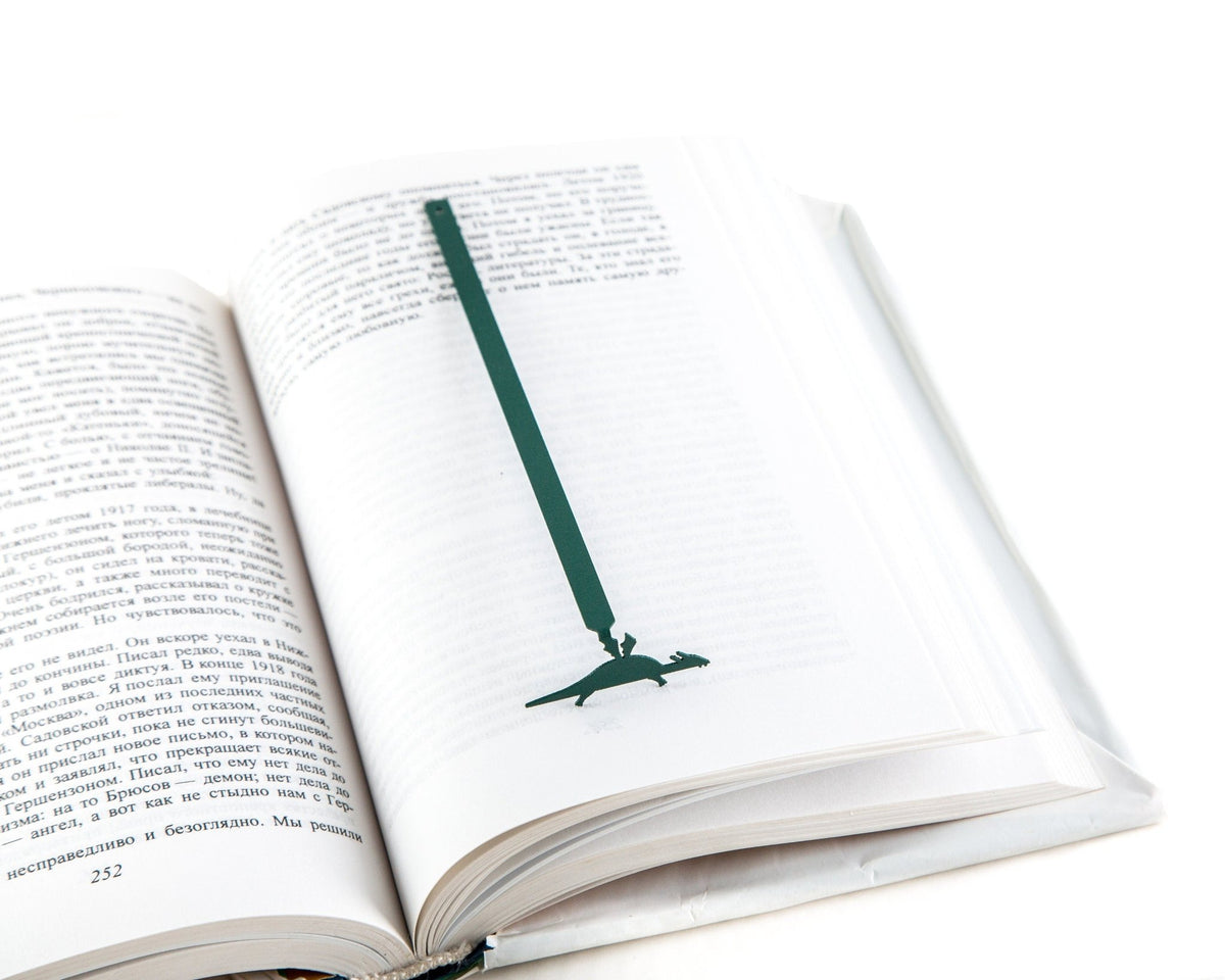 Baby Dinosaur metal bookmark in green lying across the pages of an open book