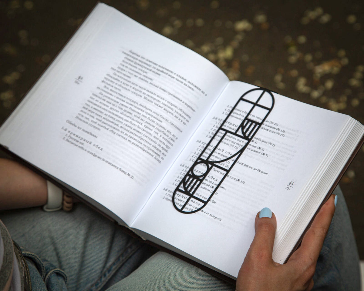 Bauhaus Geometry metal bookmark held in a hand above an open book