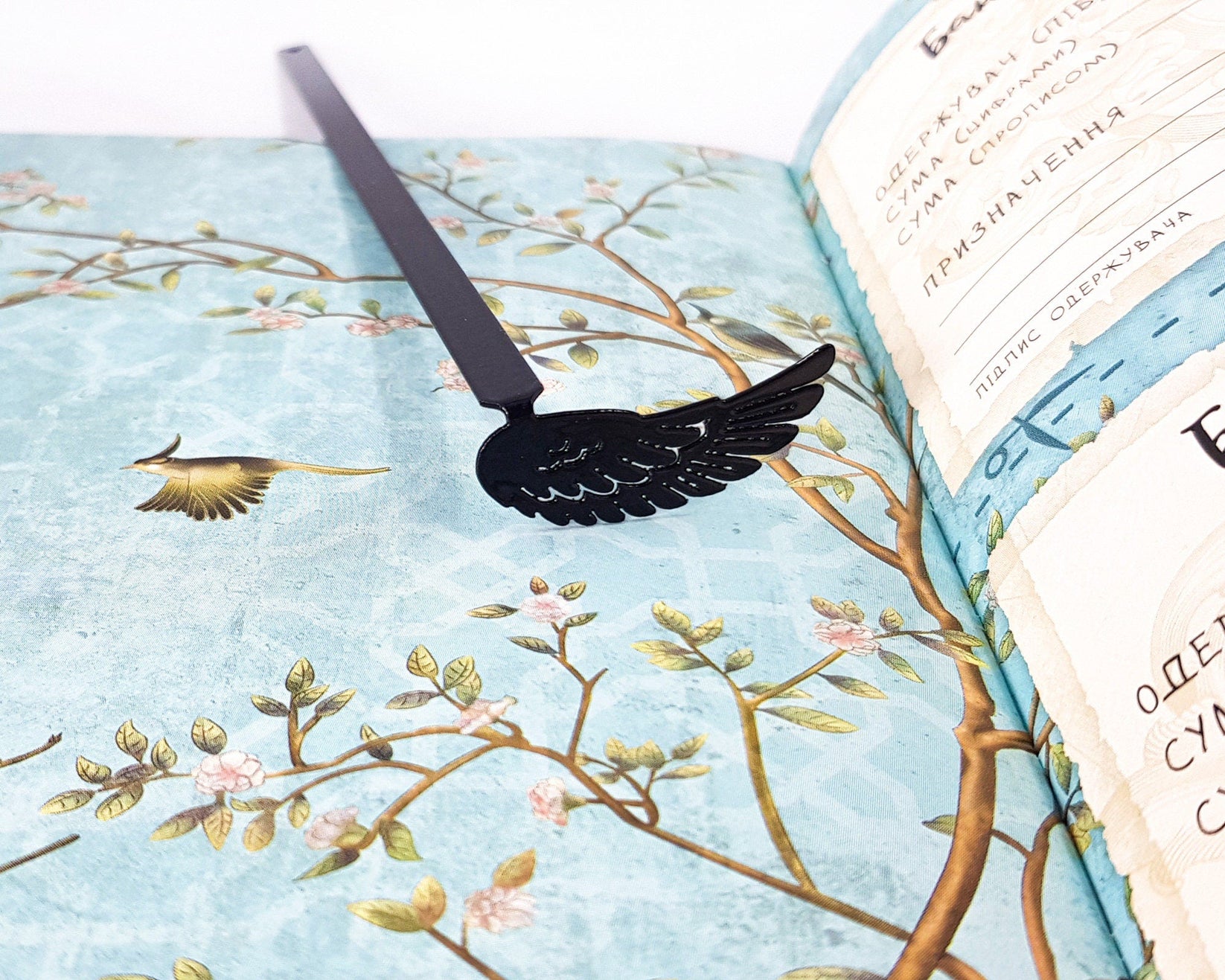 Black Wing metal bookmark marking a page in an illustrated book, view 4