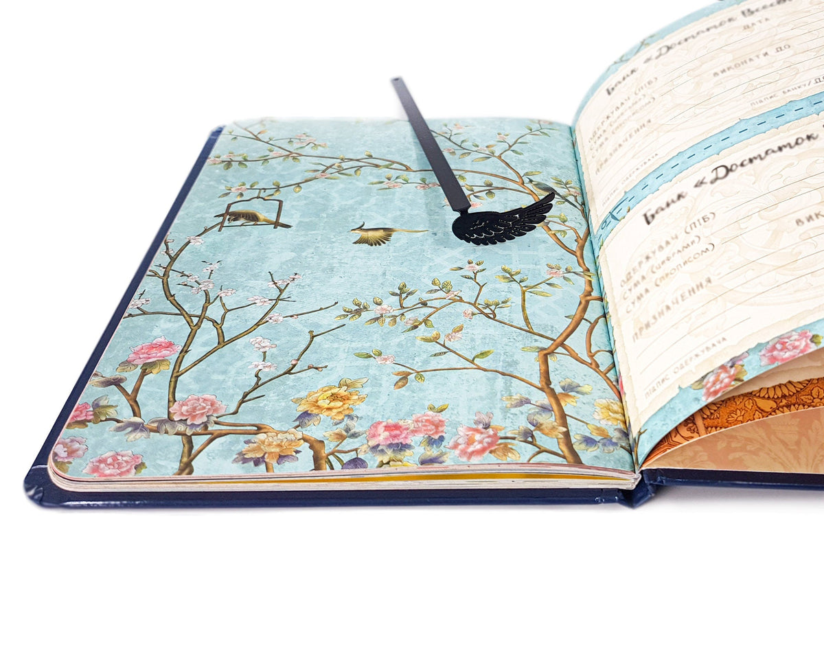 Black Wing metal bookmark placed on a colour illustration