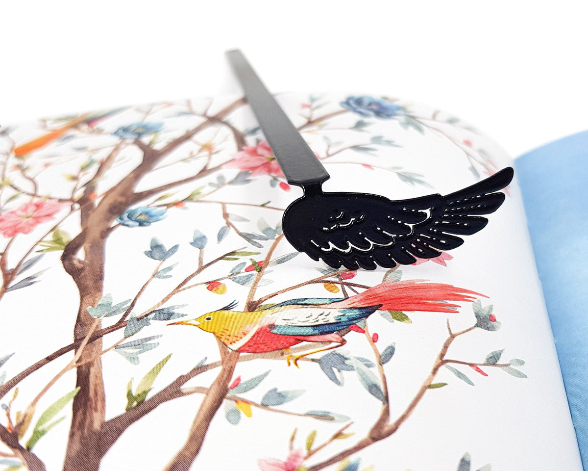 Black Wing metal bookmark marking a page in an illustrated book