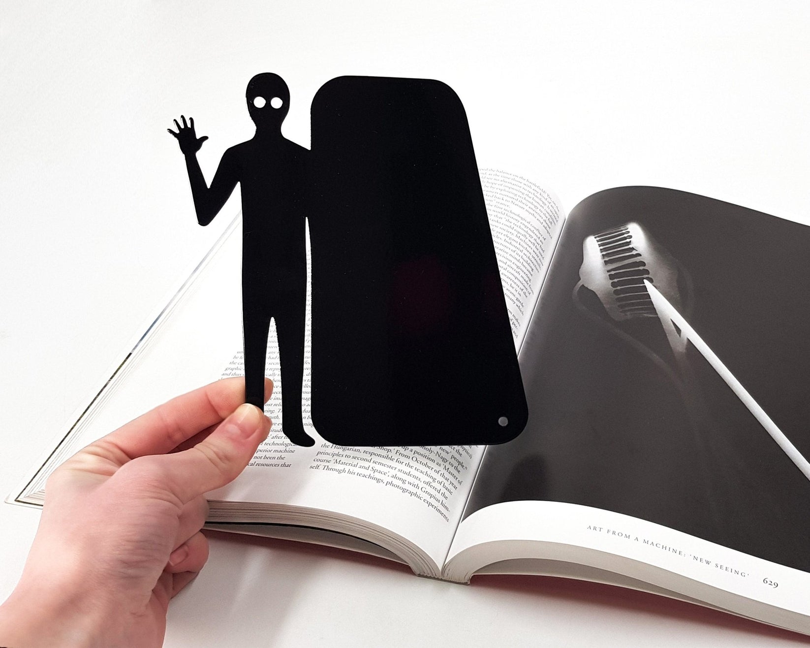 Book Ghost Coming Out metal bookmark held up beside an open book