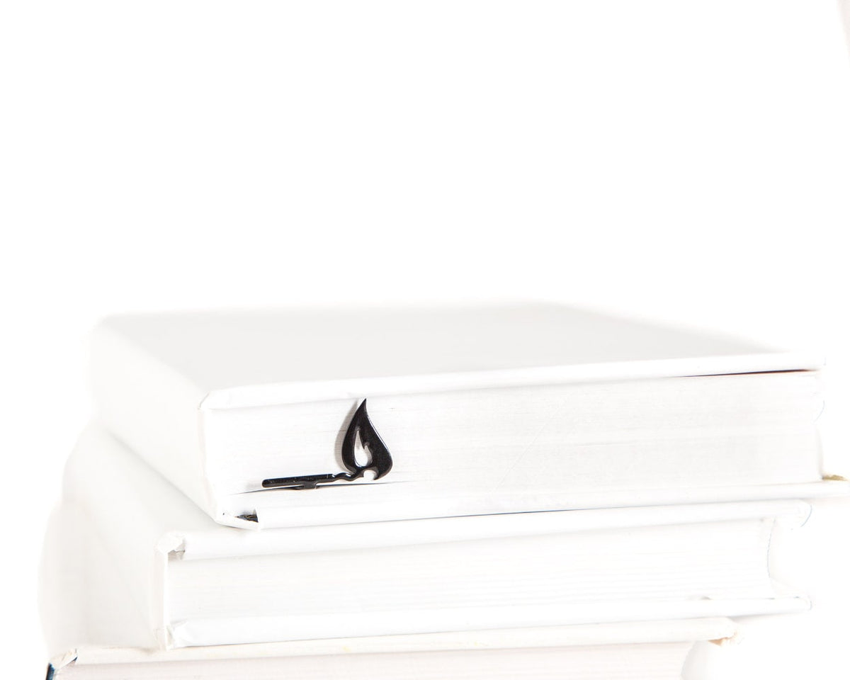 Burning Lucifer Match metal bookmark shown with a stack of books