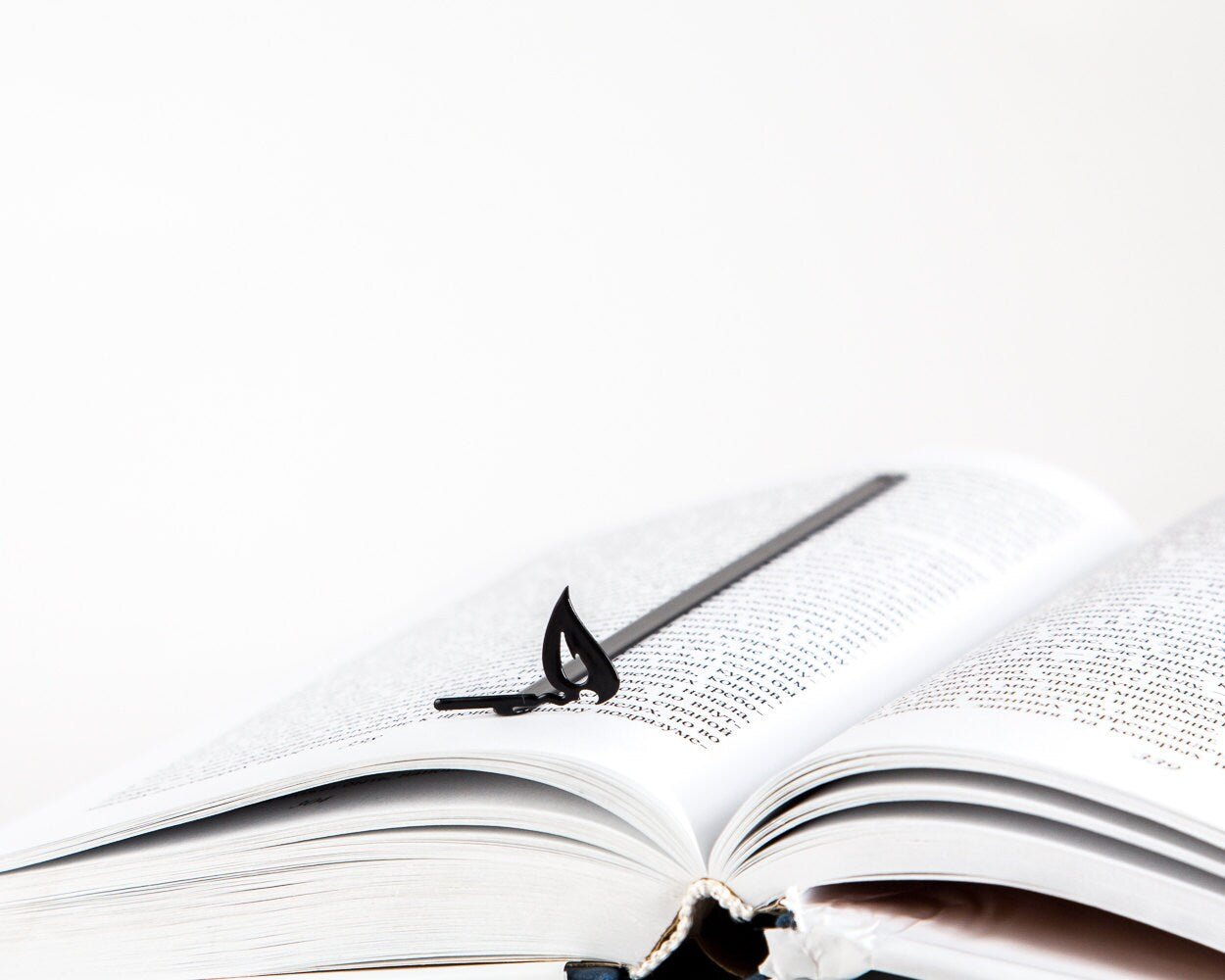 Burning Lucifer Match metal bookmark resting on the pages of an open book