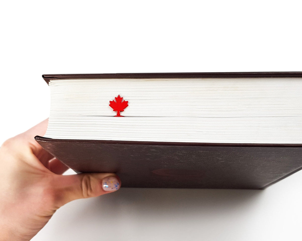 Canadian Maple Leaf metal bookmark in red held up beside an open book