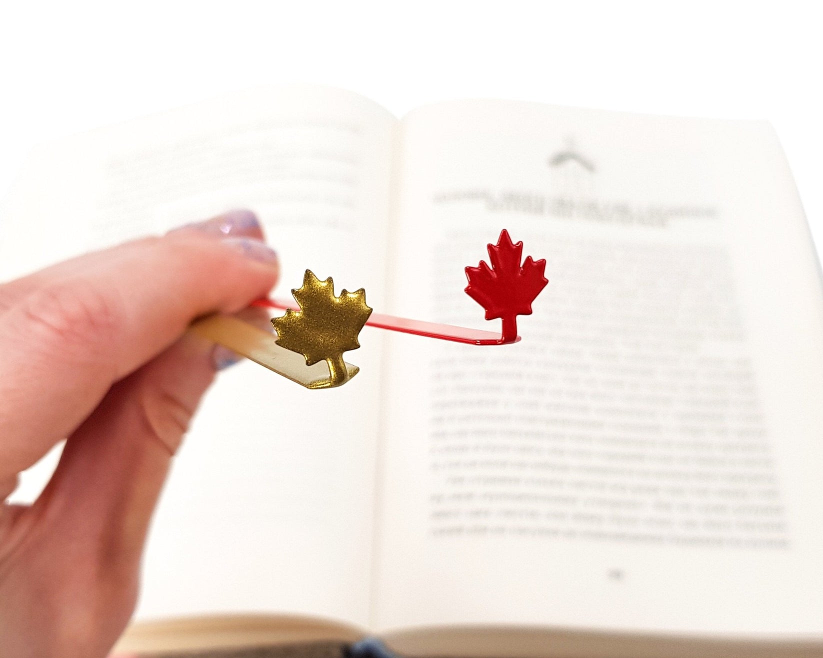 Canadian Maple Leaf metal bookmark in red held in a hand above an open book