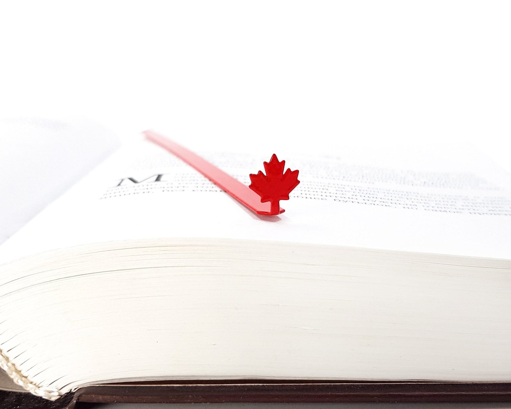 Canadian Maple Leaf metal bookmark in red lying across the pages of an open book