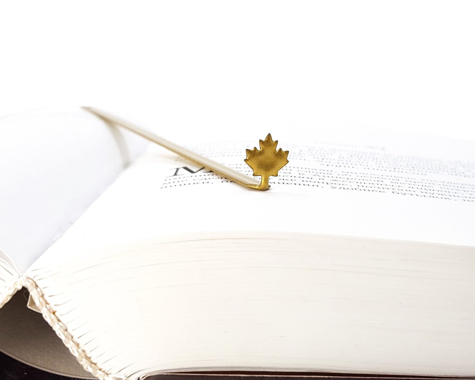 Canadian Maple Leaf metal bookmark in red resting on the pages of an open book