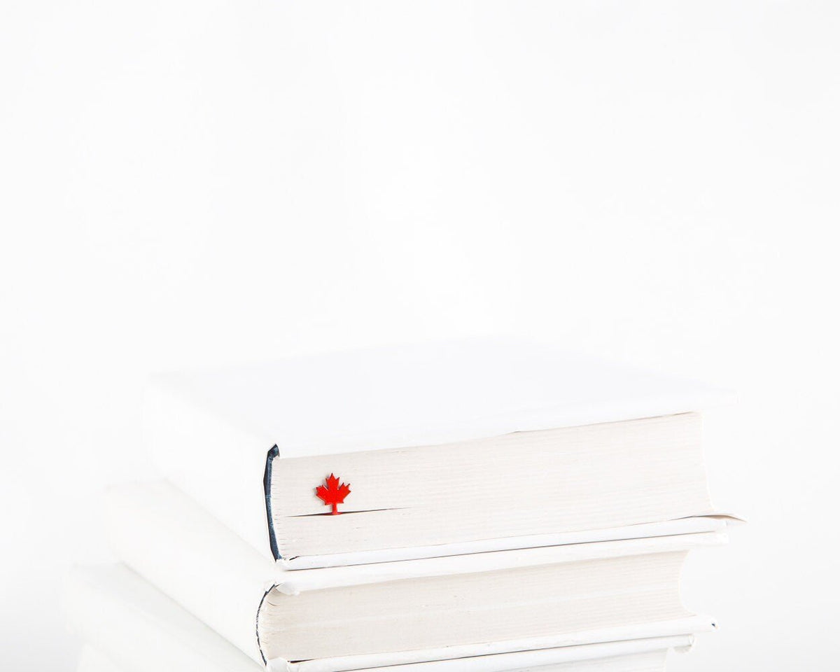 Canadian Maple Leaf metal bookmark in red in a closed book, only its top showing above the pages