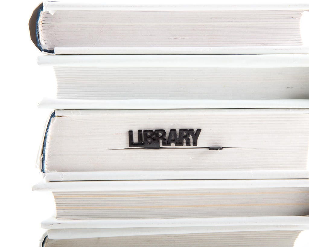 Cat's Library metal bookmark shown with a stack of books