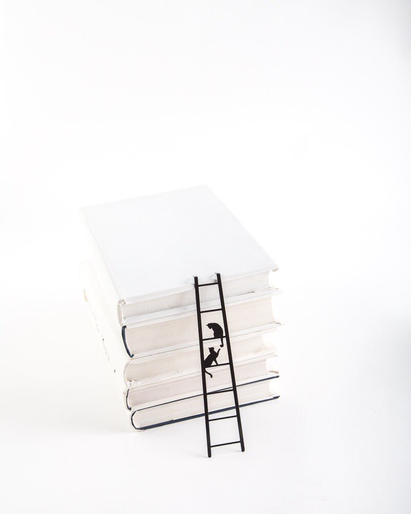 Cats on the Ladder metal bookmark in a closed book, only its top showing above the pages
