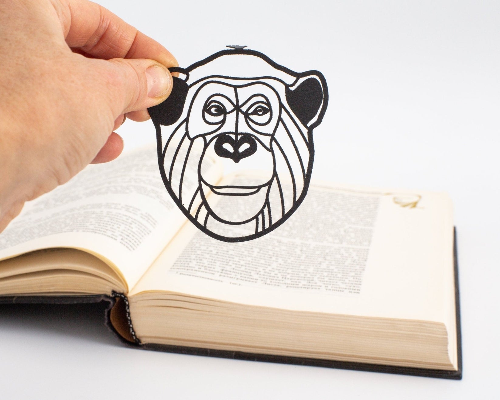 Chimp metal bookmark held in a hand above an open book