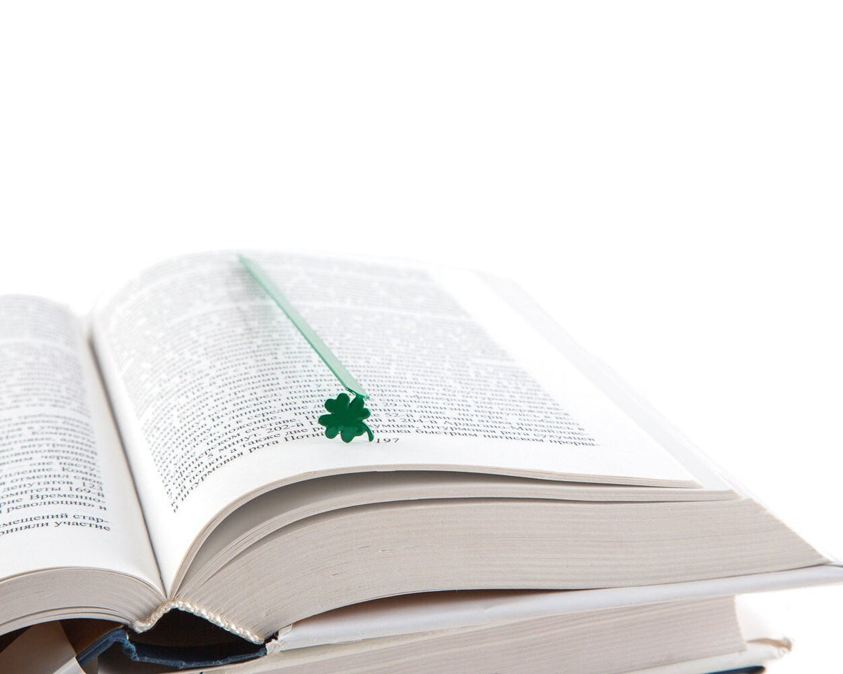 Clover, Good Luck metal bookmark in green resting on the pages of an open book