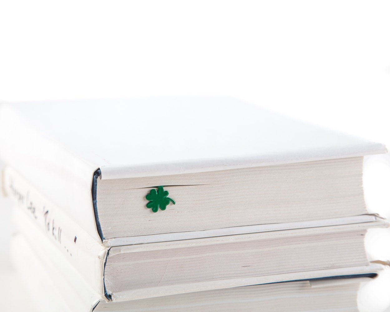 Clover, Good Luck metal bookmark in green in a closed book, only its top showing above the pages