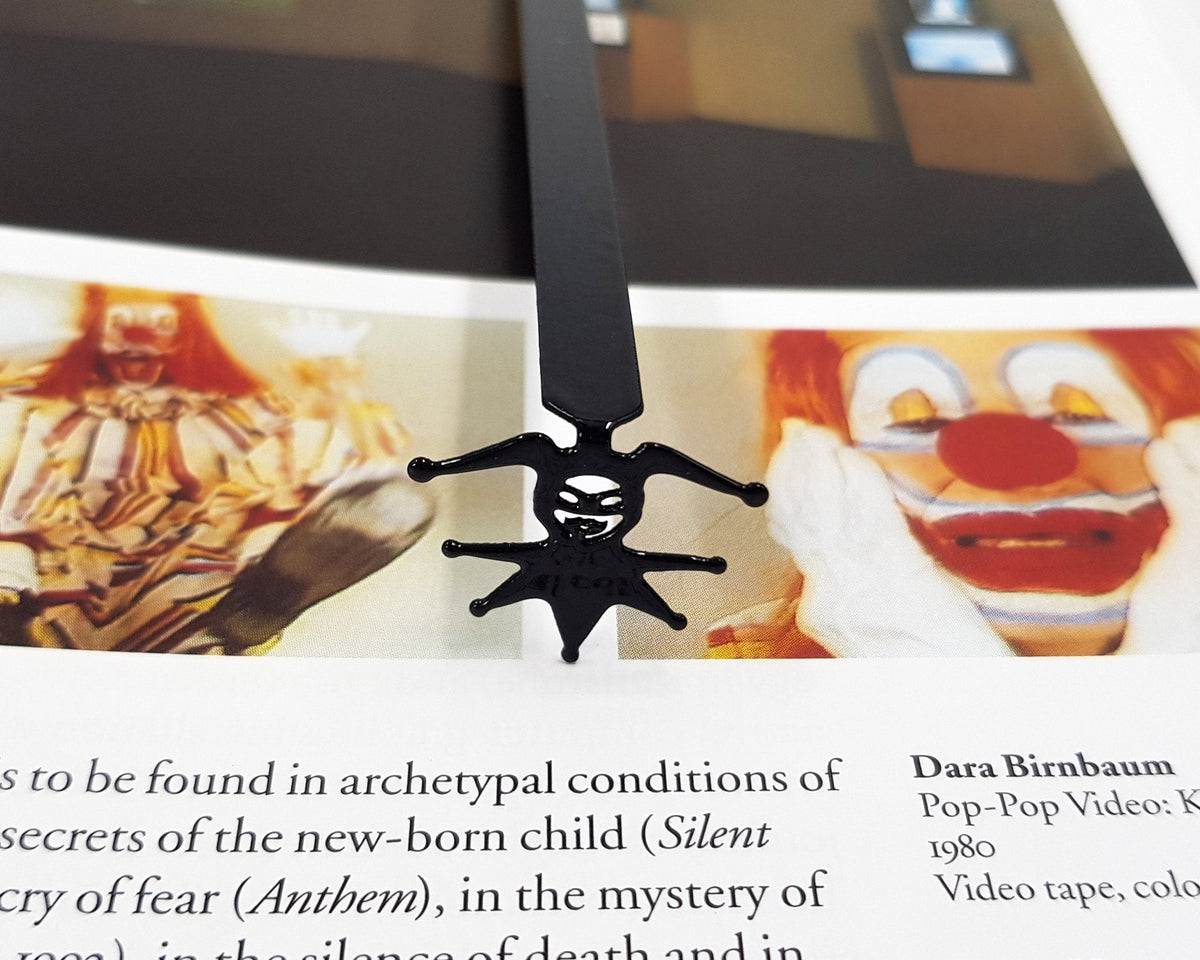 Court Jester metal bookmark marking a page in an illustrated book, view 4