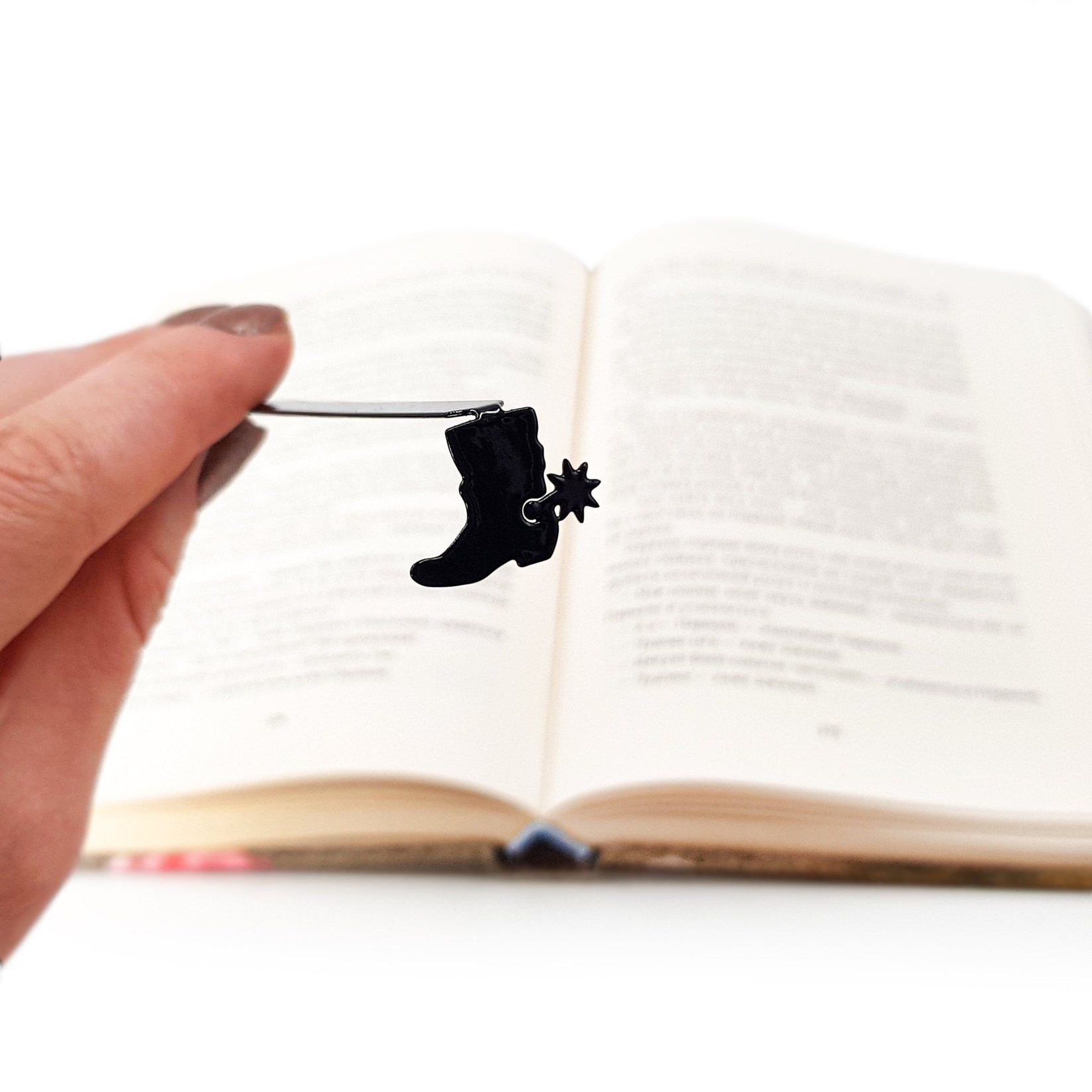 Cowboy's Boot metal bookmark held in a hand above an open book