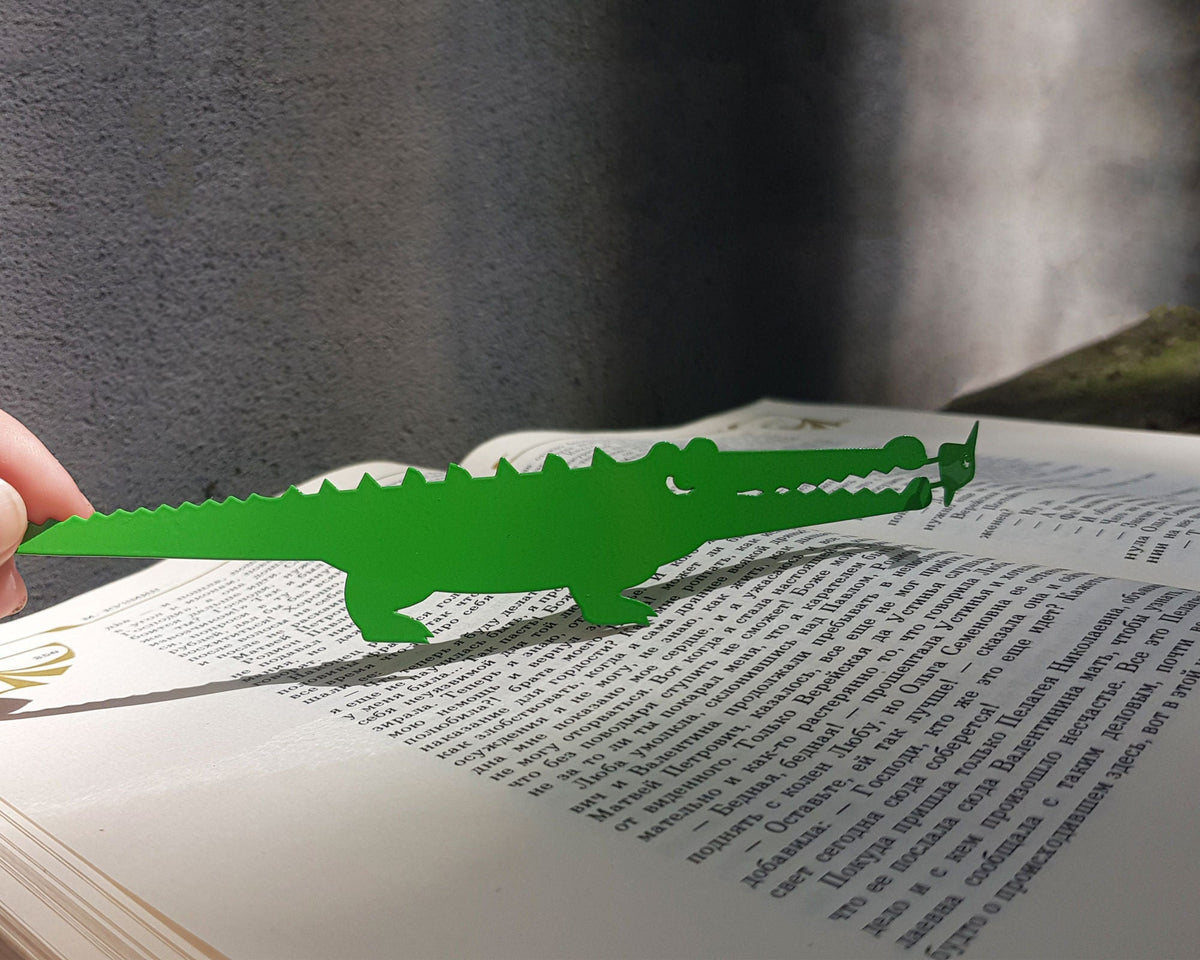 Crocodile and the Nile Bird metal bookmark in green lying across the pages of an open book
