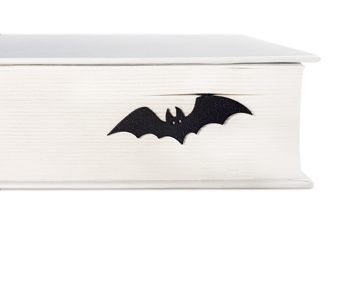 Cryptic Bat metal bookmark in a closed book, only its top showing above the pages