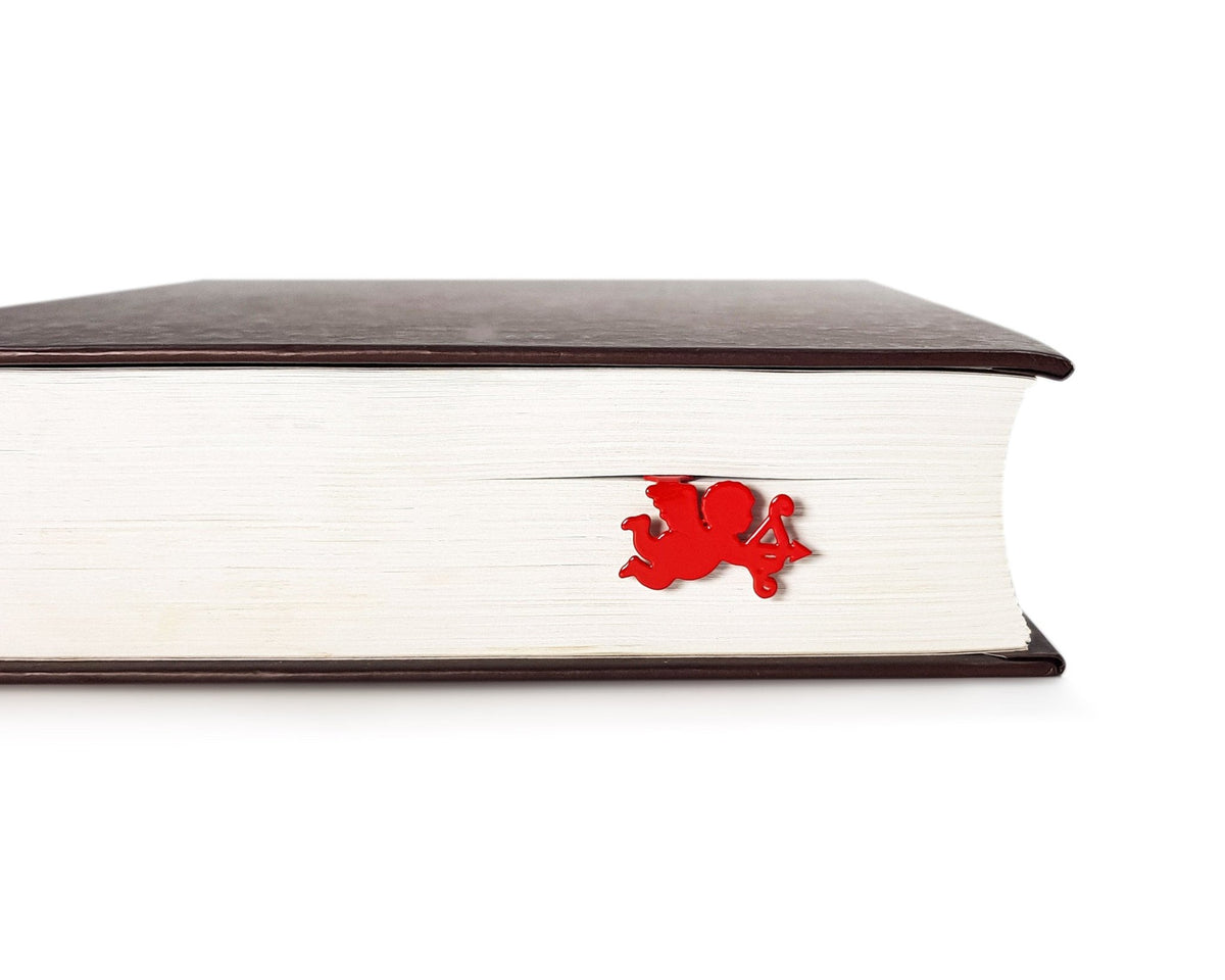 Cupid metal bookmark in red in a closed book, only its top showing above the pages