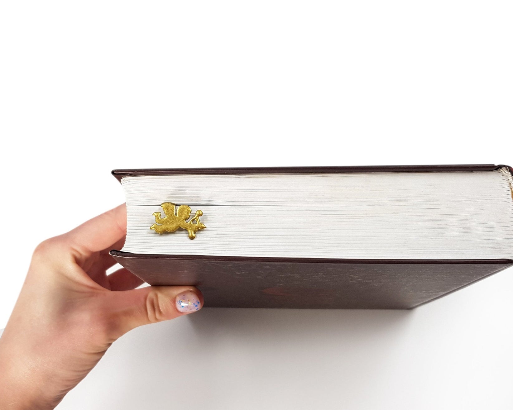Cupid metal bookmark in gold seen from the edge of a closed book