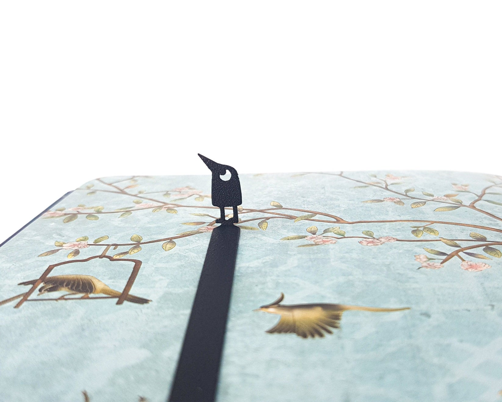 Curious Bird metal bookmark on an illustrated page