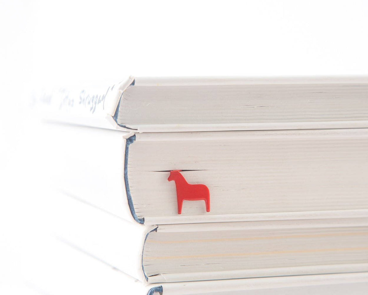 Dala Horse metal bookmark in red shown with a stack of books