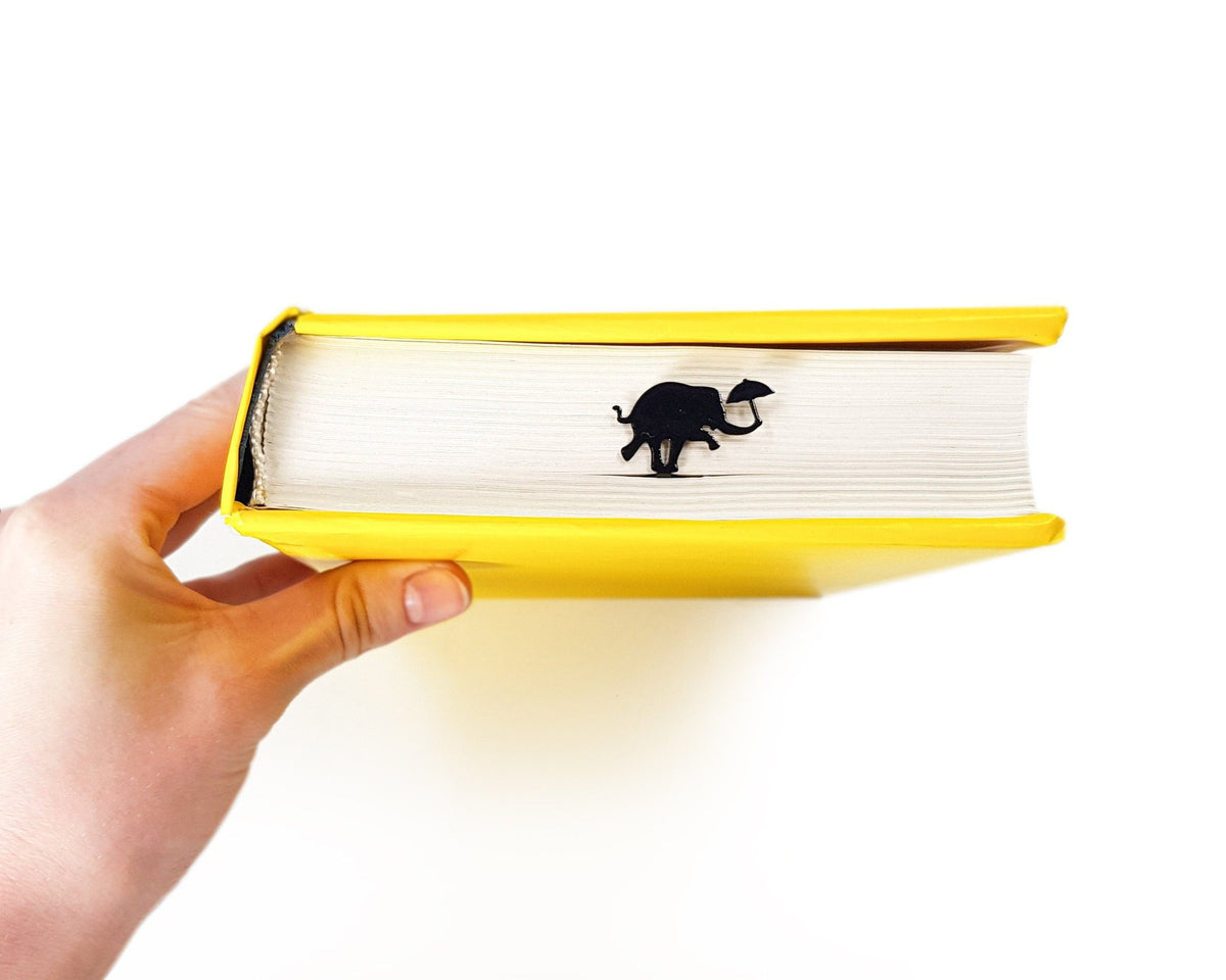 Dancing Elephant metal bookmark in a closed book, only its top showing above the pages