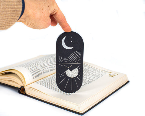 Day and Night, Sun and Moon metal bookmark held in a hand above an open book