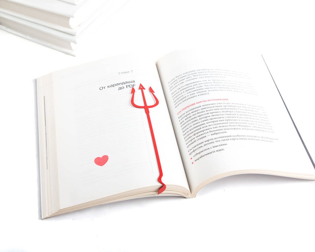 Devil's Trident metal bookmark in red marking a page in an open book