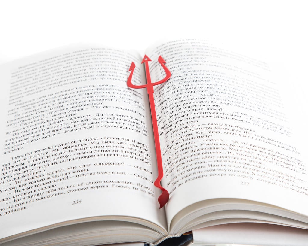 Devil's Trident metal bookmark in red resting on the pages of an open book