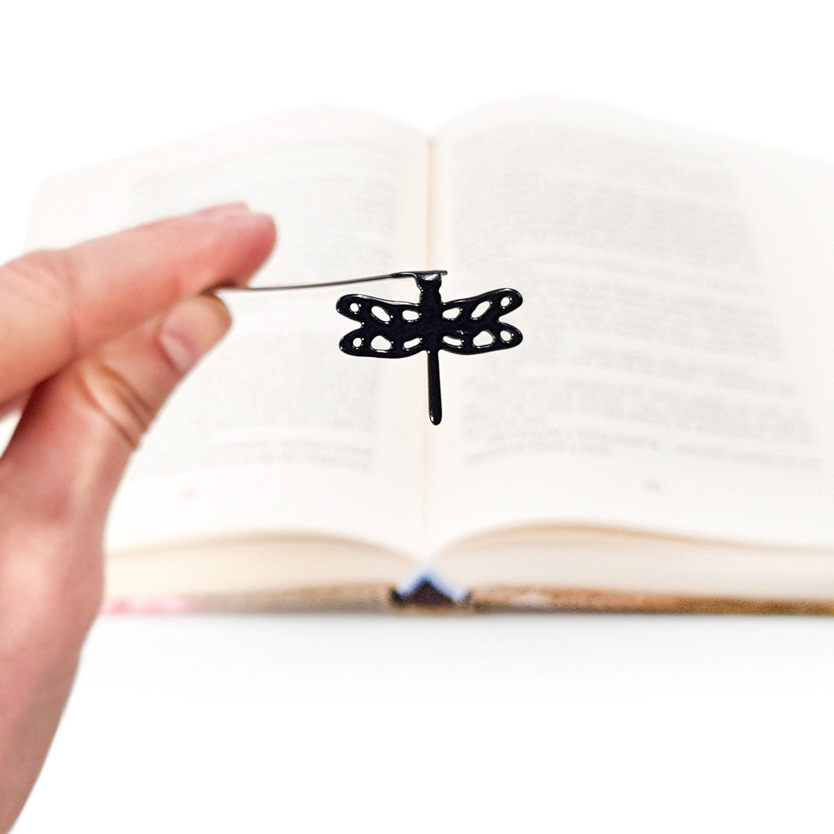 Dragonfly metal bookmark held in a hand above an open book